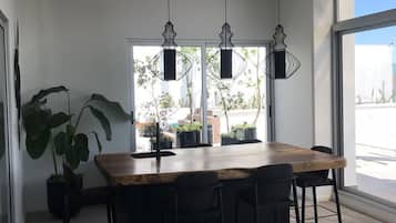 A modern dining area with a wooden table and black chairs, large windows, and hanging pendant lights.