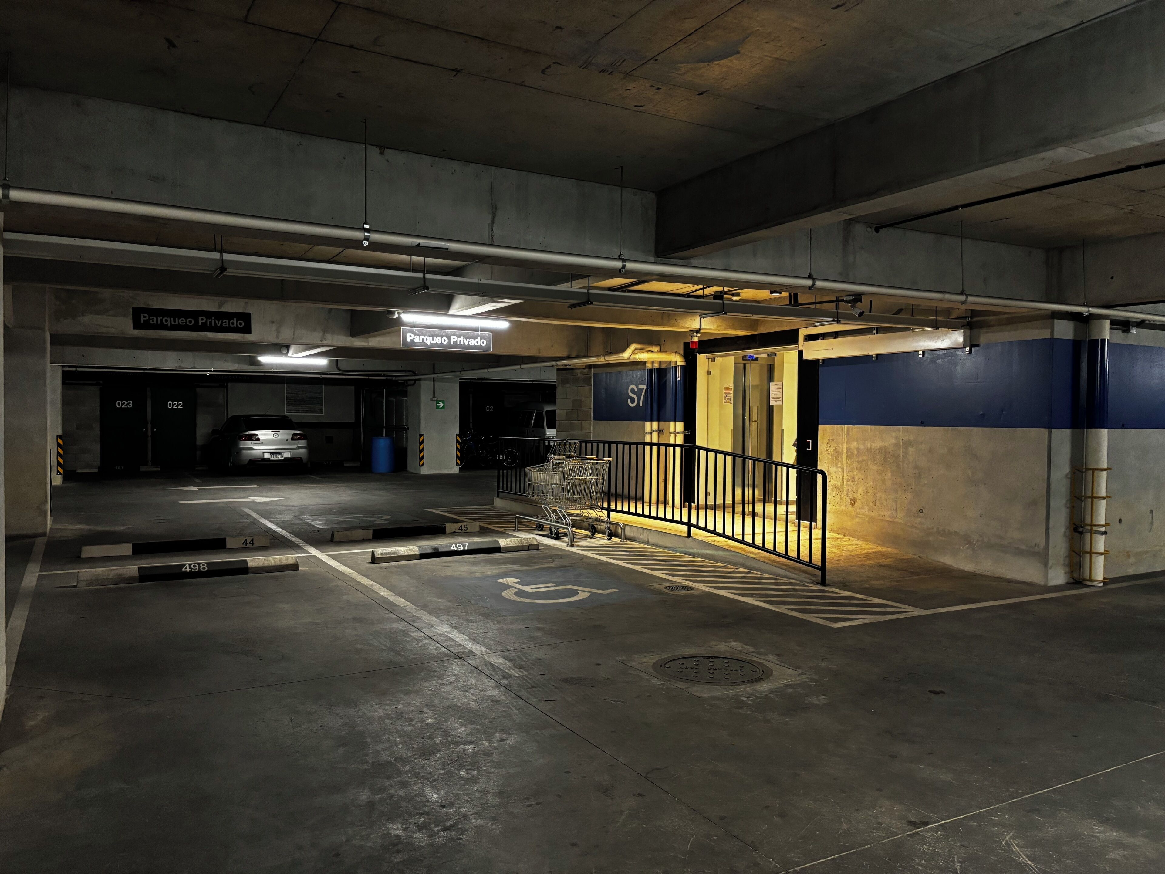 Un estacionamiento con varios niveles, espacios de estacionamiento delimitados y una escalera que lleva a un nivel superior.