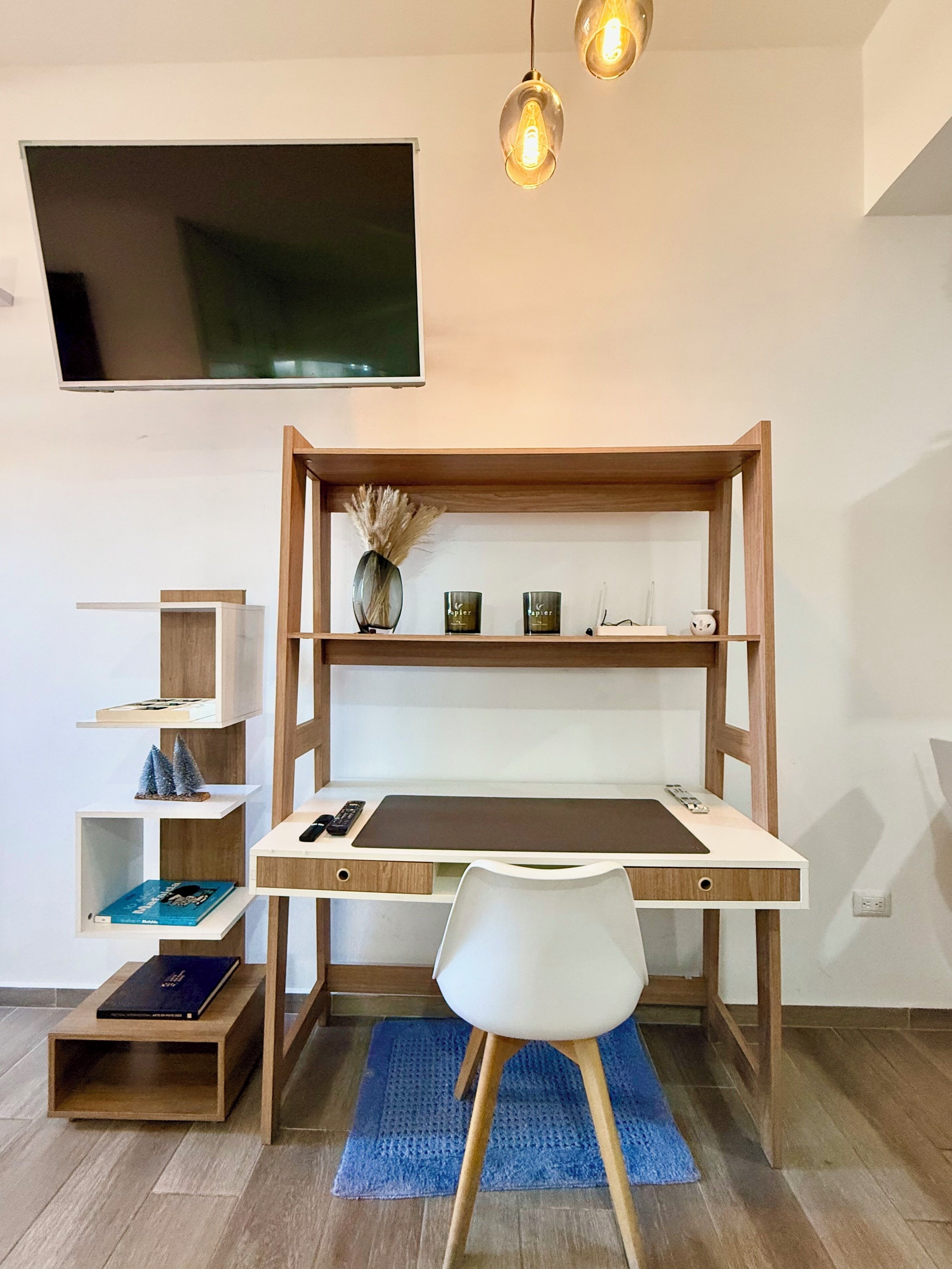 A modern study area with a wooden desk, shelves, a TV, and a blue rug.