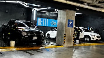 A parking garage with a black car being washed, a white car parked nearby, and a blue sign indicating a parking area.