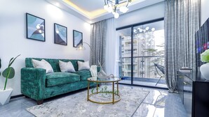 Una sala de estar moderna con un sofá azul verdoso, una mesa de centro de vidrio y un gran ventanal con cortinas.