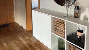 Ein modernes Zimmer mit einer Holztür, einem weißen Schrank mit Körben, einem runden Spiegel und einem kleinen Regal mit Dekoration.