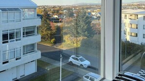 Blick aus einem Fenster auf ein Wohngebiet mit einem weißen Gebäude, einer Straße mit Autos und blauem Himmel.