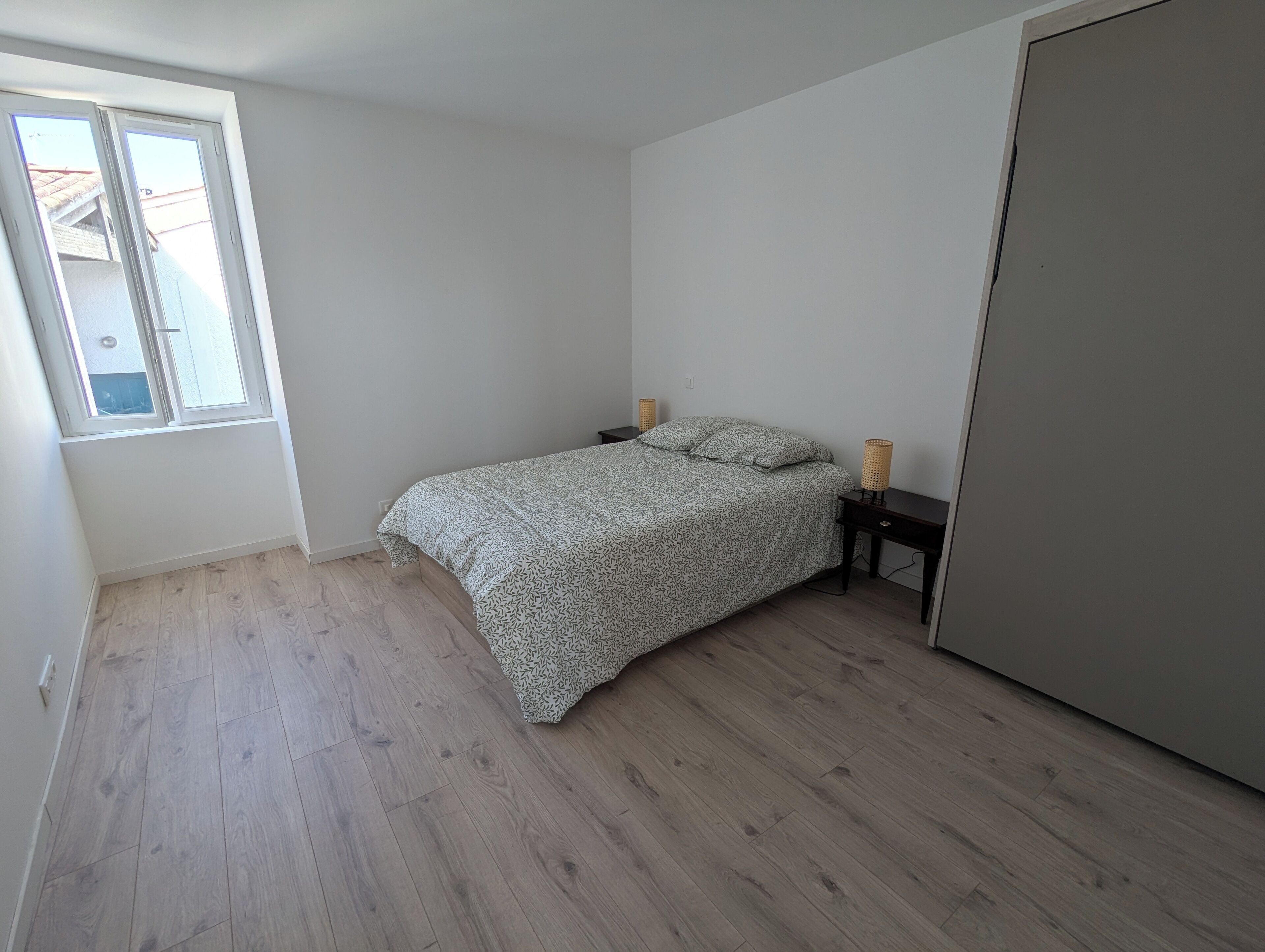A bedroom with a bed, two bedside tables, a wardrobe, and a window.