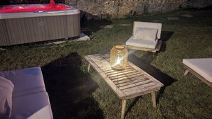 A hot tub, two lounge chairs, and a table with a lantern in a grassy outdoor area.