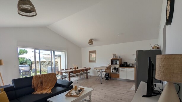A spacious living area with a sofa, coffee table, and a dining table with chairs. A kitchen with a microwave and stove is visible in the background.