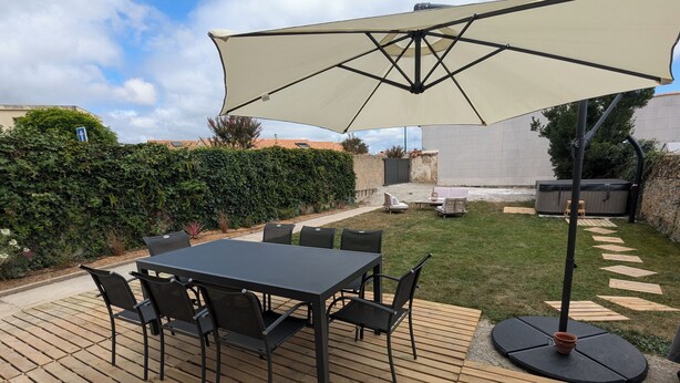 Une terrasse avec une table et des chaises, un grand parasol et un jacuzzi.