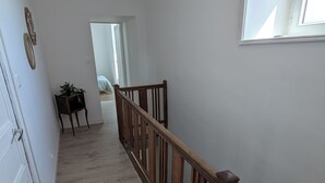 A hallway with wooden flooring, a wooden railing, and a door on the left.