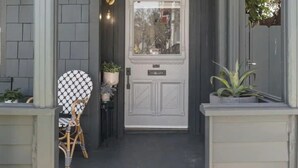 A gray door with a white frame, a small porch with a chair and potted plants, and a brick pathway leading to the door. - 4BR (Sleeps 10!)Heart of Little Italy: Walk to Dining & Fun! (San Diego)