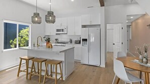 A modern kitchen with white cabinets, a central island with stools, and pendant lighting. - 4BR (Sleeps 10!)Heart of Little Italy: Walk to Dining & Fun! (San Diego)