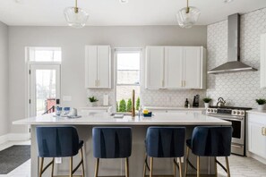 A modern kitchen with white cabinets, a central island with bar stools, and a large stove.