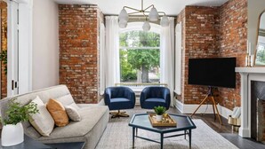 Una sala de estar con pared de ladrillo, un sofá, dos sillones, una mesa de centro, un televisor de pantalla plana y una chimenea.