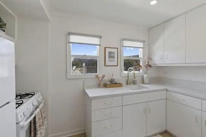 Una cocina con armarios blancos, una estufa y dos ventanas.