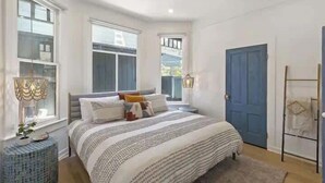 Ein Schlafzimmer mit einem Bett, Nachttischlampen, einer blauen Tür und einem Fenster mit Blick.