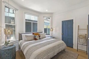 Un dormitorio con una cama grande, dos mesitas de noche, un armario y una puerta.