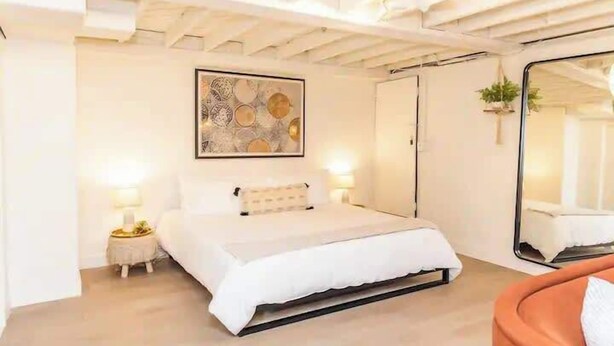 A bedroom with a bed, bedside tables, a large mirror, and a wall art piece.