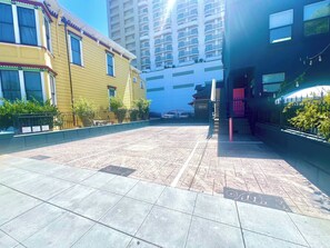 A courtyard with tiled flooring, a yellow building with a red trim, and a tall blue building in the background.