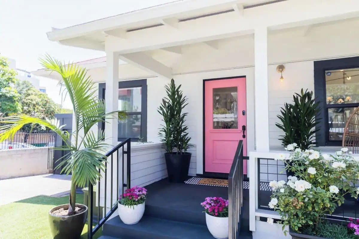 Ein Haus mit Veranda, einer rosafarbenen Tür und Kübelpflanzen.