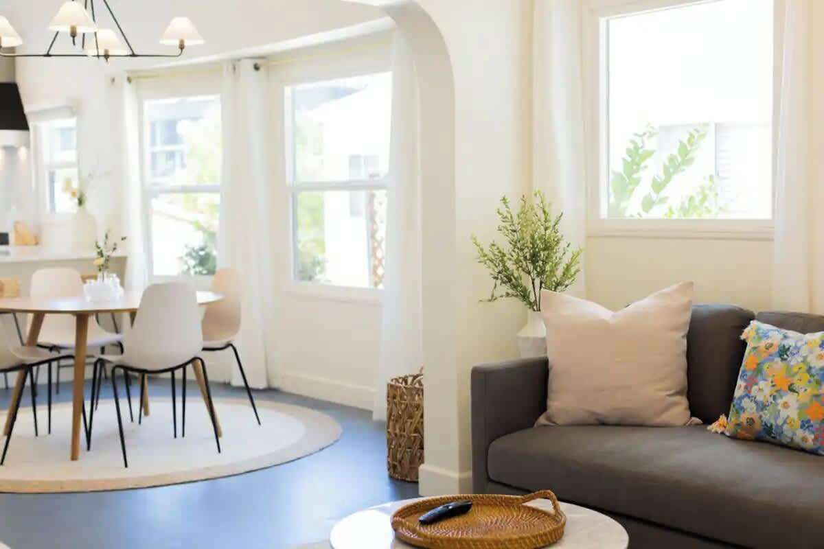 Ein modernes Wohnzimmer mit grauem Sofa, einem Esstisch mit Stühlen und einem großen Fenster, das natürliches Licht hereinlässt.