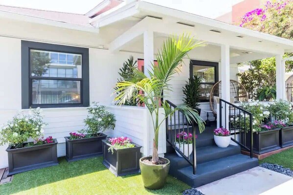 Une maison moderne dotée d’un porche abrité, de plantes en pot et d’un escalier menant à l’entrée.