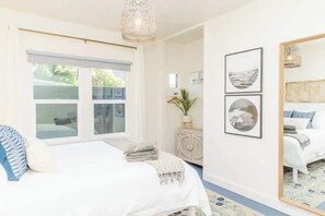 Une chambre à coucher avec un lit, une fenêtre, un miroir et des œuvres d’art murales.
