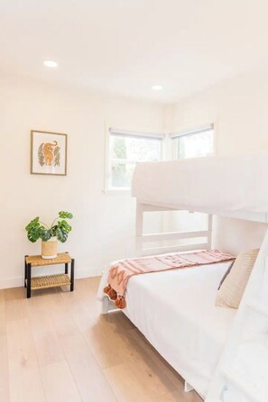 A bunk bed room with a window, a plant on a small table, and a framed picture on the wall. - Bright 4BR Little Italy Home: Free Parking & Sleeps 9! (San Diego)