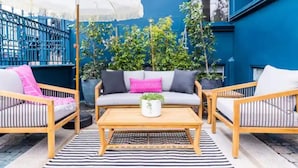 An outdoor seating area with a wooden table, two sofas, and a white umbrella. - Bright 4BR Little Italy Home: Free Parking & Sleeps 9! (San Diego)