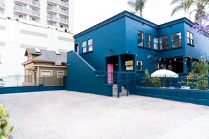 A two-story building with a blue exterior, a gated entrance, and a small garden area with a white structure.