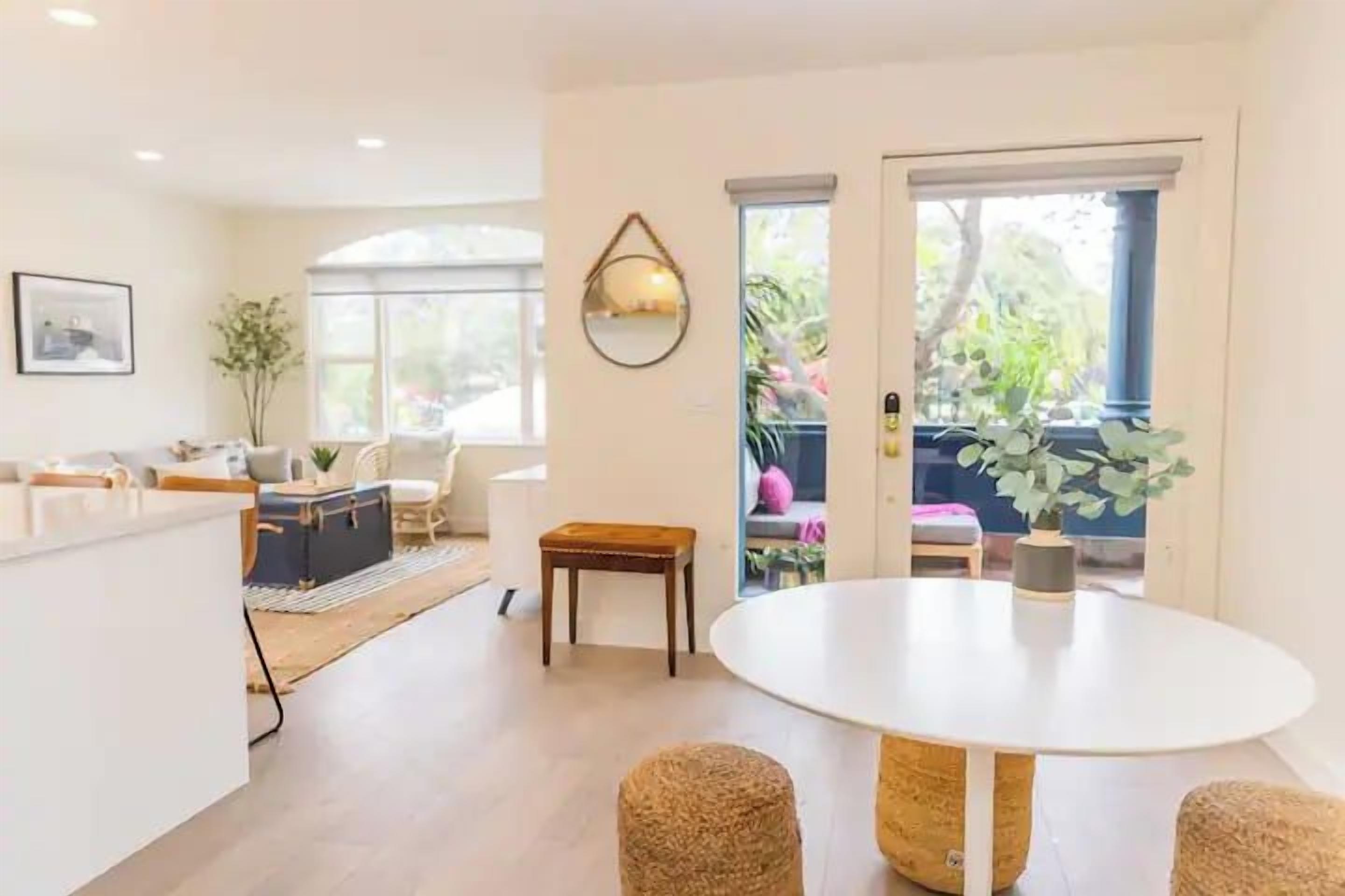 A modern living room with a round dining table, a sofa set, and a view through a glass door.