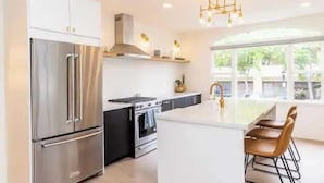A modern kitchen with stainless steel appliances, a central island with bar stools, and a large window providing natural light. - Bright 4BR Little Italy Home: Free Parking & Sleeps 9! (San Diego)