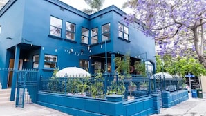 A blue building with a white awning, a fenced garden area, and a tree with purple flowers. - Bright 4BR Little Italy Home: Free Parking & Sleeps 9! (San Diego)