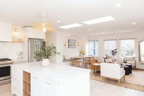Una cocina moderna con una isla central, zona de comedor con una mesa y sillas de madera, y sala de estar con sofá y mesa de centro.