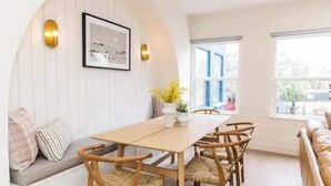 Spiseområde med et træbord og stole, en bænk med hynder samt et billede hængt på væggen.