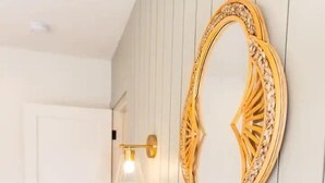 Et soveværelse med en seng, hvide vægge, et træsengegærde, et spejl på væggen og en sengetårnslampe.