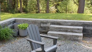 A seating area with Adirondack chairs and a stone bench, surrounded by a stone wall and gravel ground, set in a forested area. - Corkscrew Cape - Family Friendly Upstate NY Escape (Barryville)