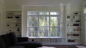 A room with a large window, built-in shelving, a dark sofa, and a round table. - Corkscrew Cape - Family Friendly Upstate NY Escape (Barryville)