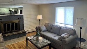 A living room with a gray sofa, a coffee table, a fireplace, and a window with blinds. - Green Mountain Access:

 (Rutland)