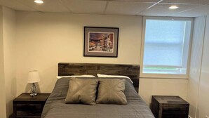 A bedroom with a bed, a nightstand, a lamp, a framed picture on the wall, and a window. - Green Mountain Access:

 (Rutland)