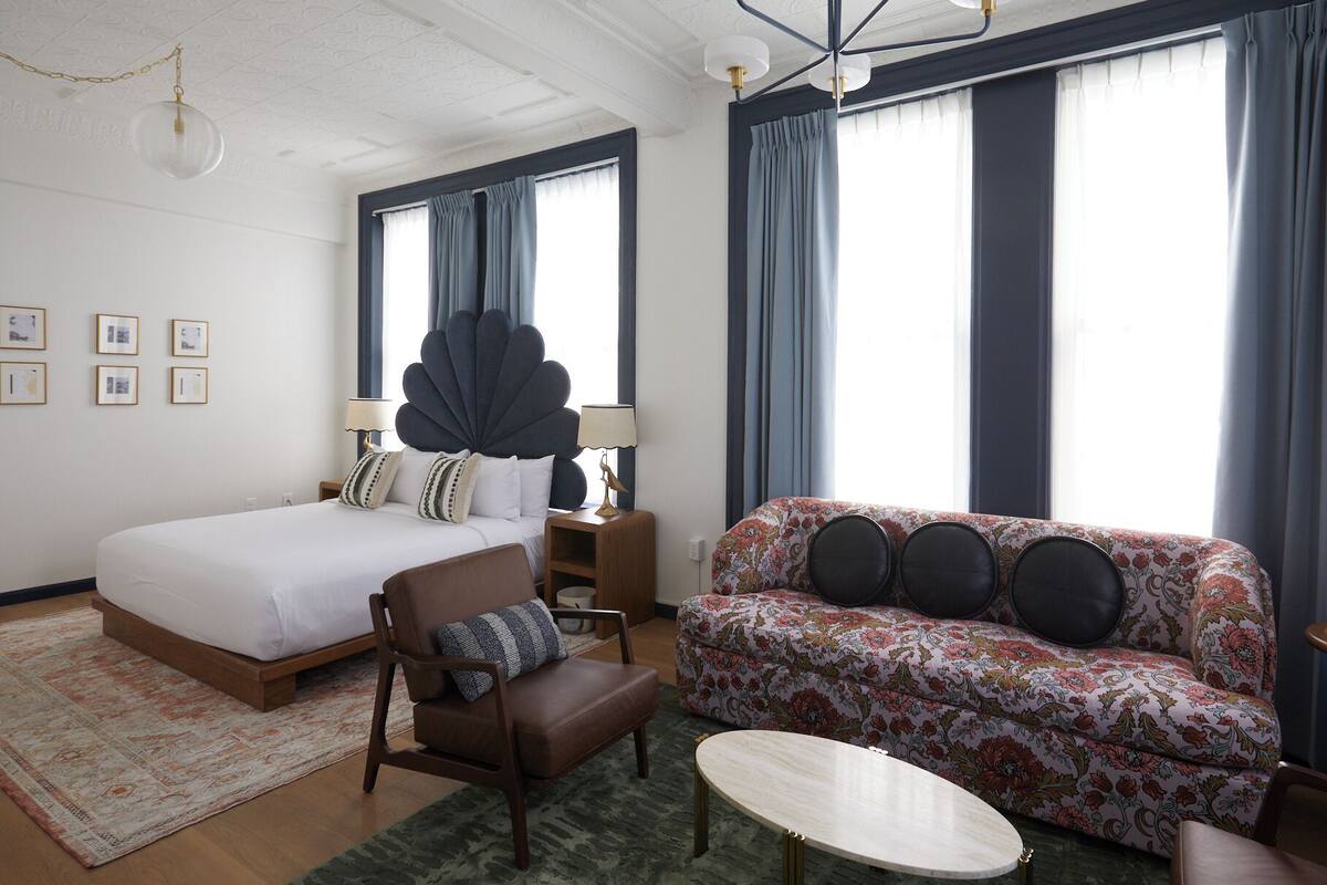 A hotel room with a large bed, a sofa, a chair, a small table, and a chandelier.