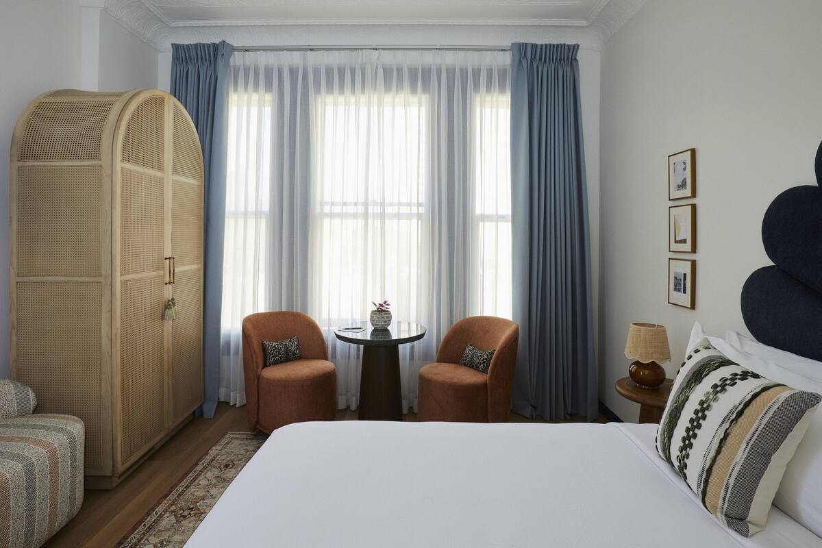 A hotel room with a large bed, two armchairs, a small table with a vase, and a rattan wardrobe.
