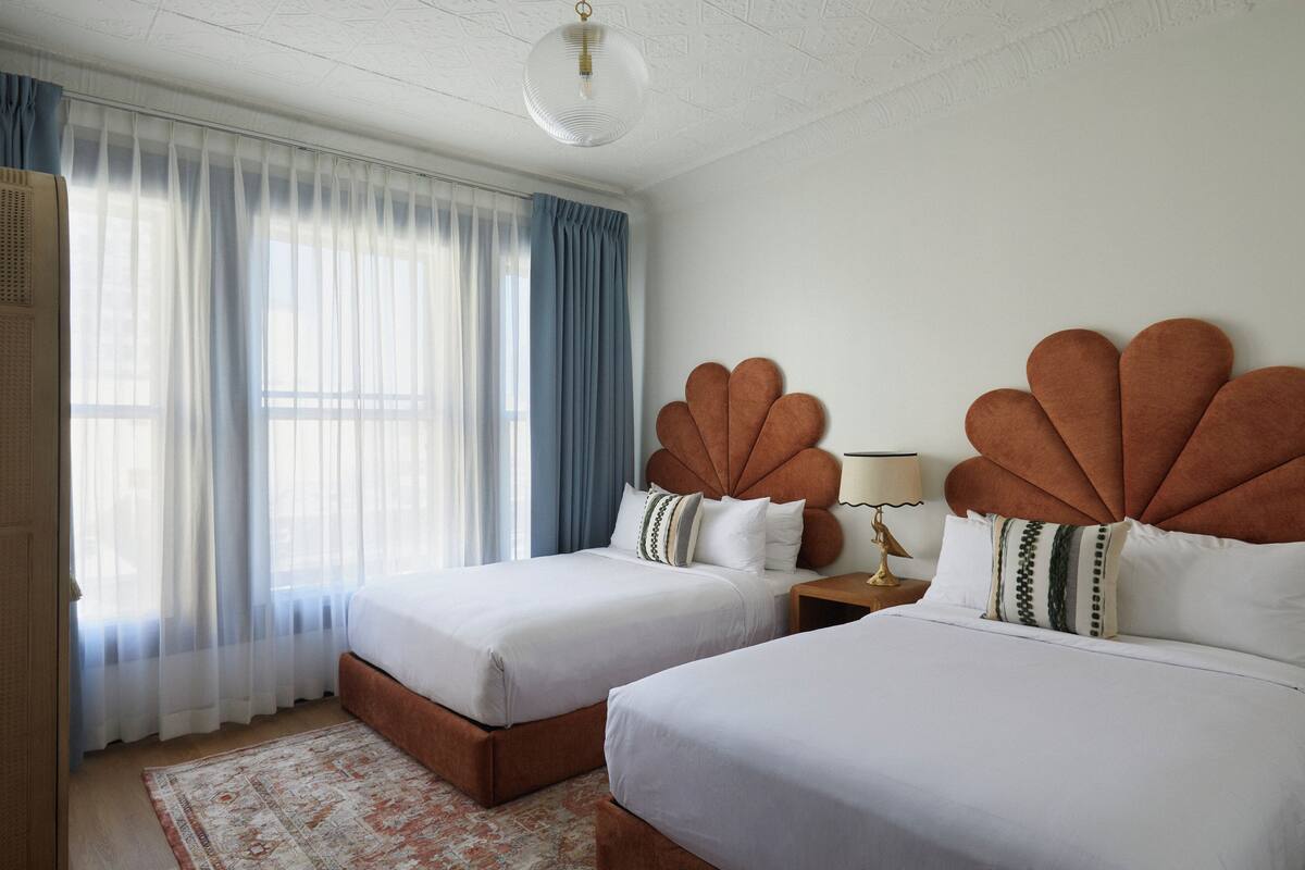 A hotel room with two beds, a large window with sheer curtains, and a patterned rug.