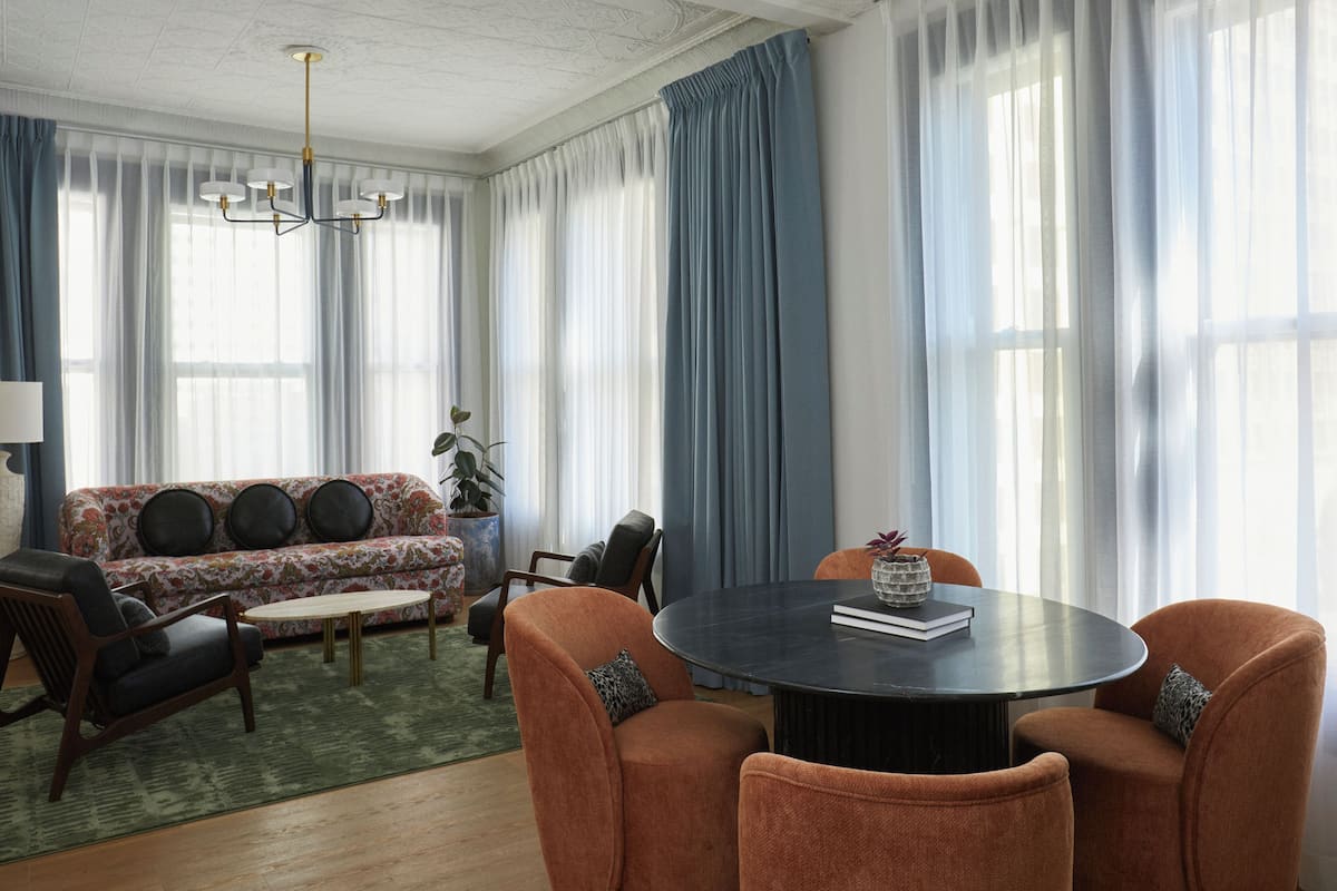 A modern living room with a round table, orange chairs, a sofa, and a chandelier.
