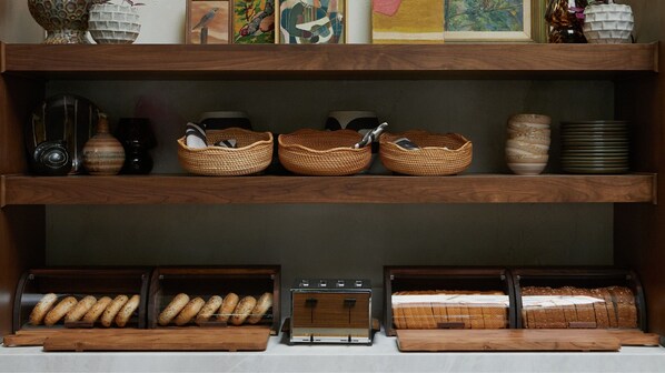 A bakery display with bread and pastries, wicker baskets, and ceramic items on shelves.