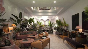 Un vaste salon doté d’un haut plafond, de plusieurs coins salon et d’une abondance de plantes d’intérieur.