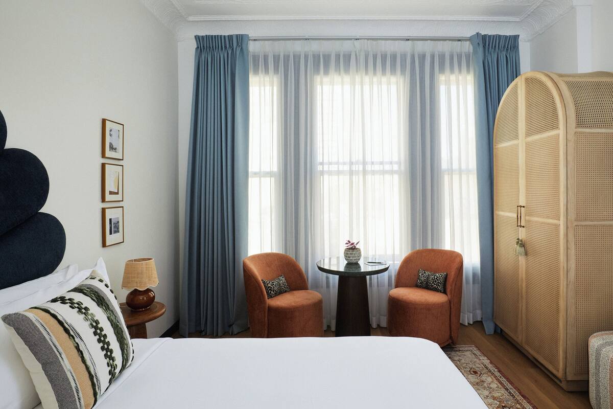 A hotel room with a large bed, two armchairs, a small table with a vase and a phone, and a wardrobe.