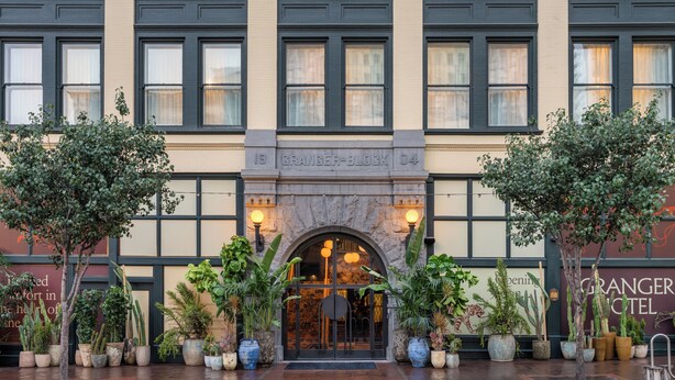 L’entrée d’un hôtel, avec une arche en pierre, de nombreuses fenêtres et des plantes en pot.