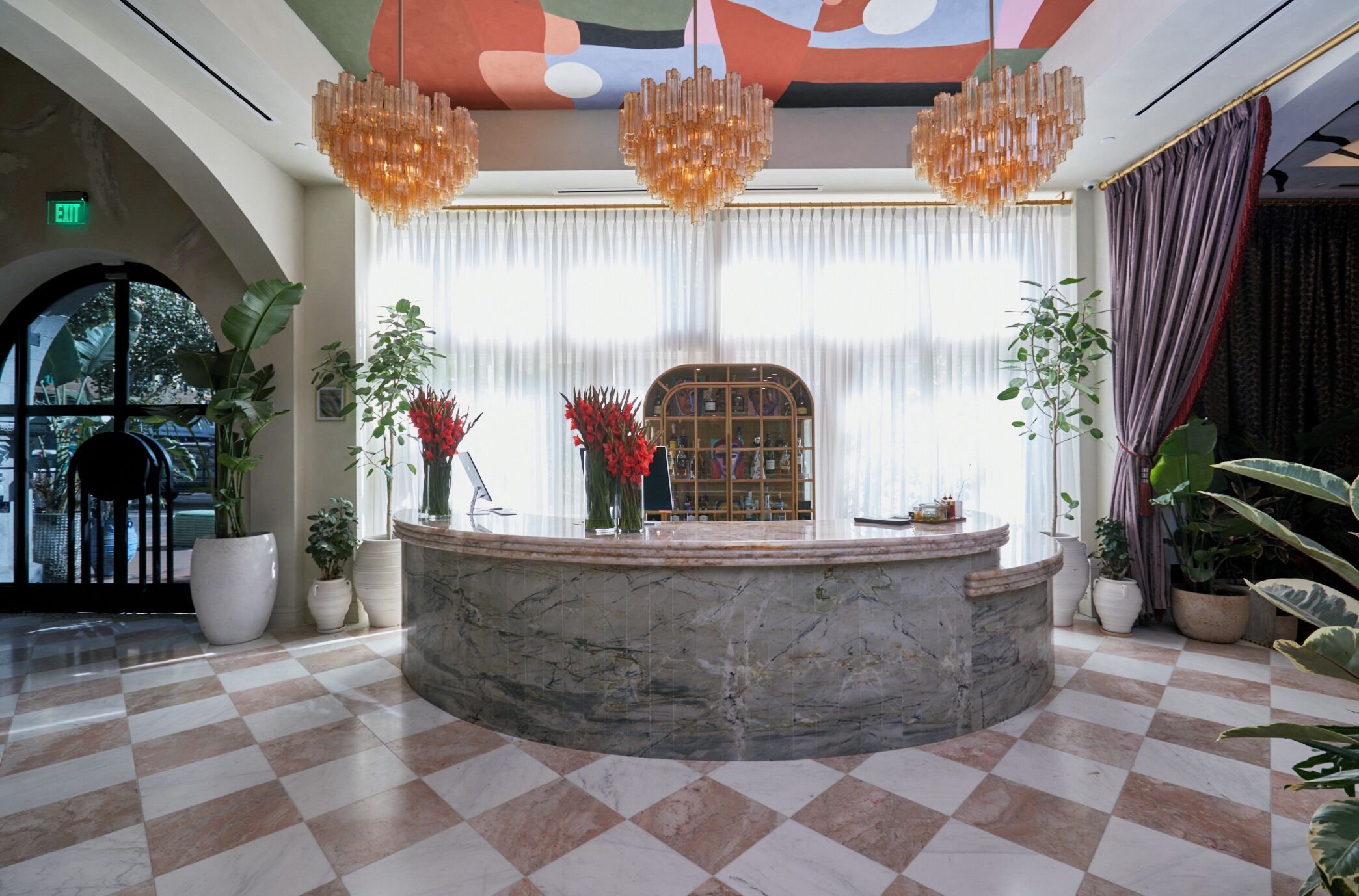 A lobby with a marble reception desk, large windows with sheer curtains, and a checkered floor.