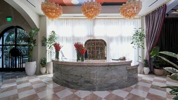 A lobby with a marble reception desk, large windows with sheer curtains, and a checkered floor.