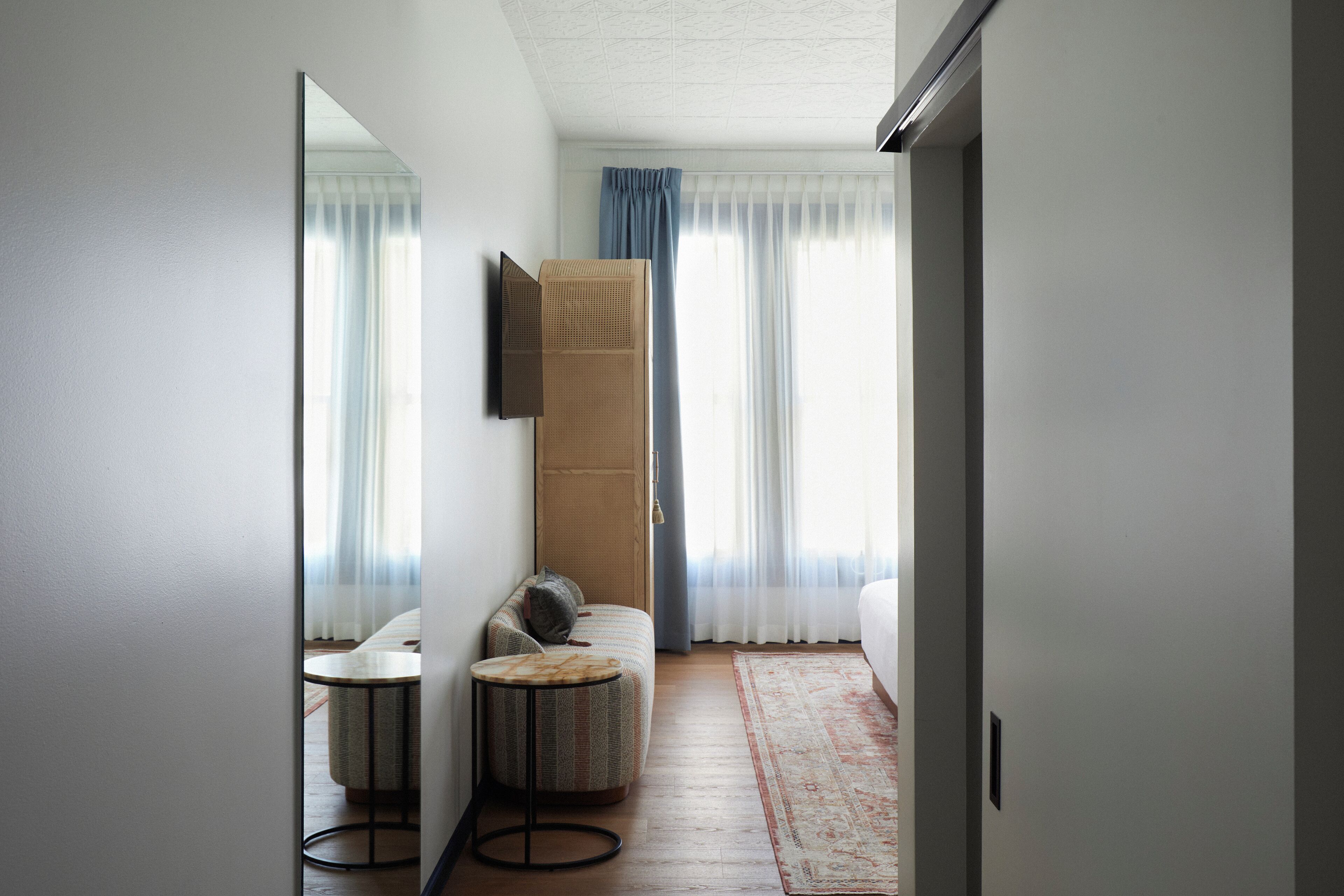 Una habitación de hotel moderna con un sofá, una pequeña mesa redonda, un espejo grande y un equipo de aire acondicionado de gran tamaño.