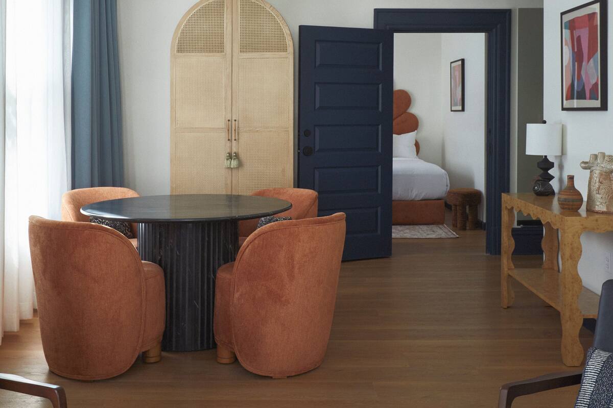 A modern living room with a round table, two orange chairs, a blue door, and a wooden floor.